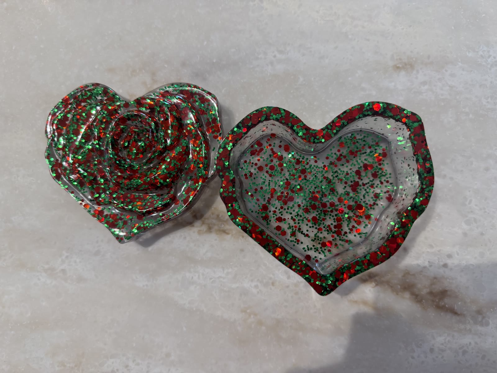 Heart-shaped resin trinket box with a 3D rose lid and matching base, both packed with red and green glitter, shown open on marble